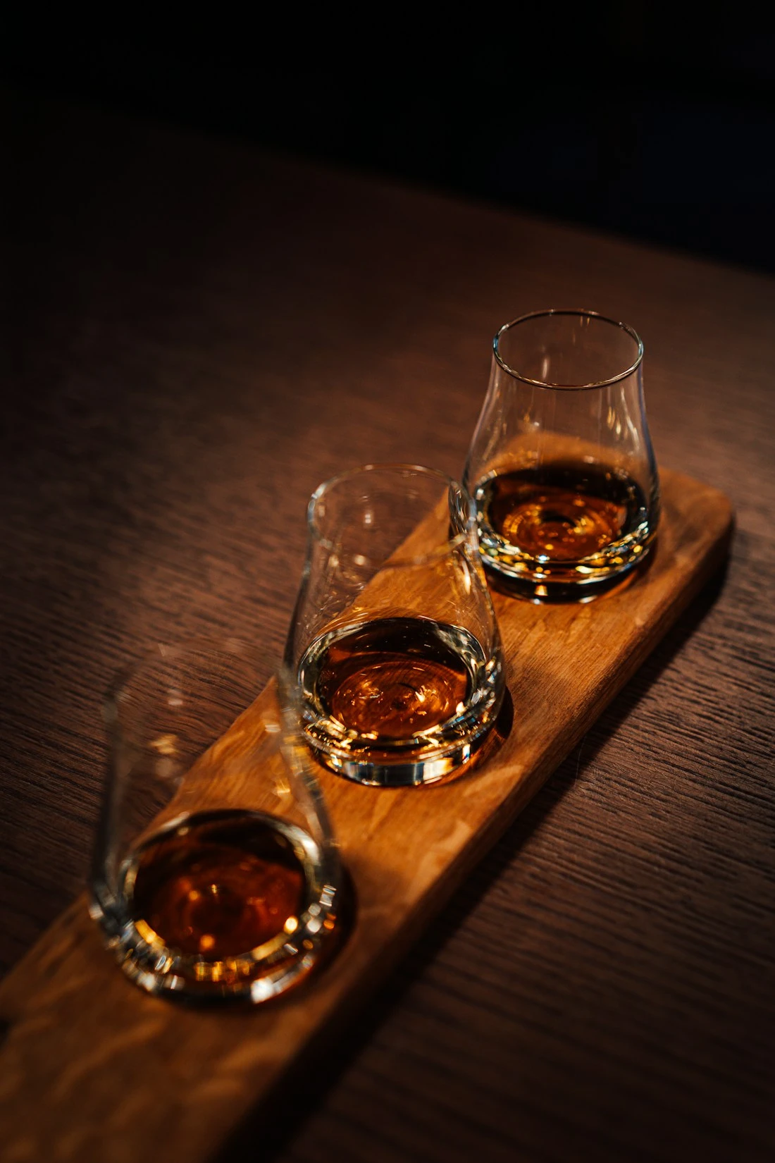 Three whiskey tasting glasses on wooden paddle